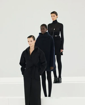 Three female models posing in dark coats and black attire against a plain white studio background.