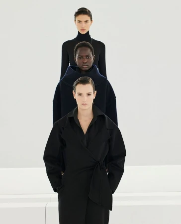 Three models standing in a straight vertical line wearing black coats against a neutral white studio background.