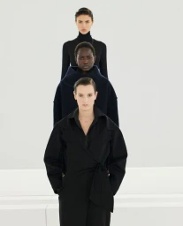 Three models standing in a straight vertical line wearing black coats against a neutral white studio background.