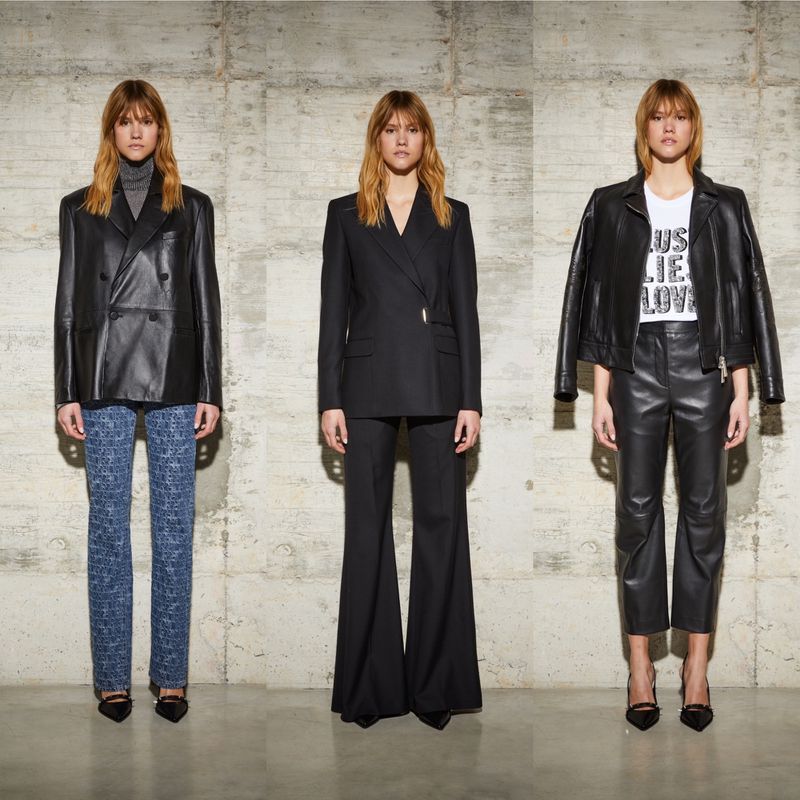 Three women model black blazers and pants in a studio setting, showcasing fashion with a focus on leather and tailored looks against a concrete wall.