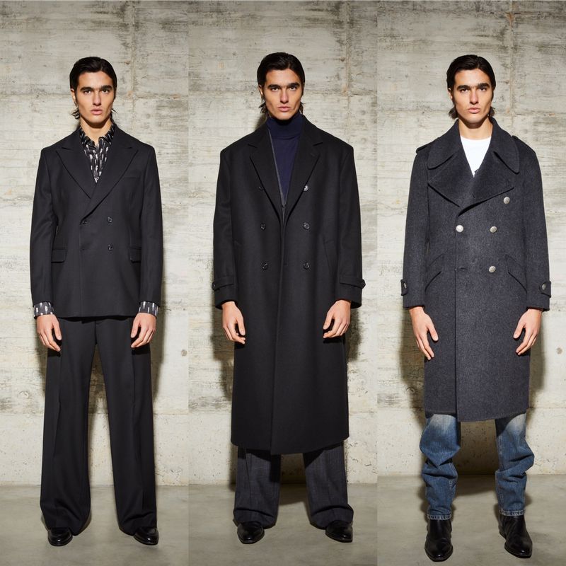 Fashion shot showcasing an adult male wearing a suit, a long coat, and a pea coat in an indoor studio environment with a textured backdrop.