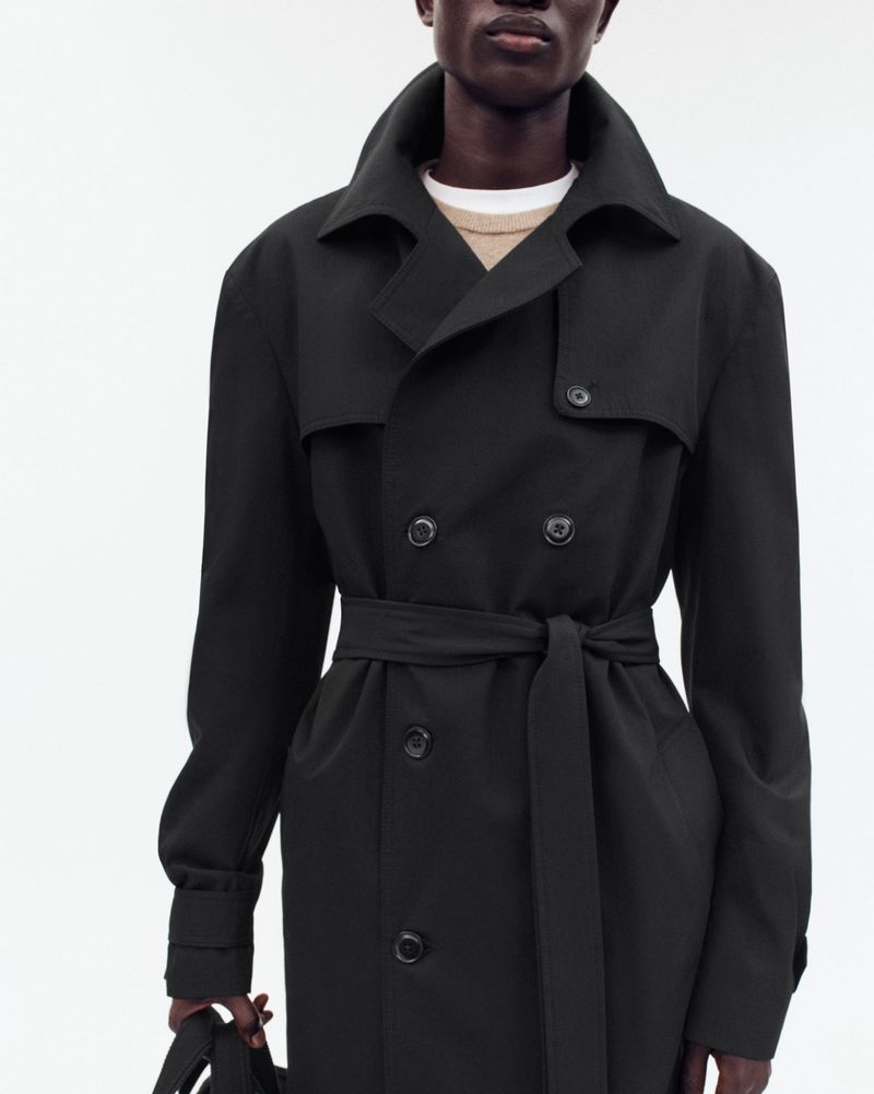 Black man wearing a dark trench coat against a white background for Zara Origins lookbook.