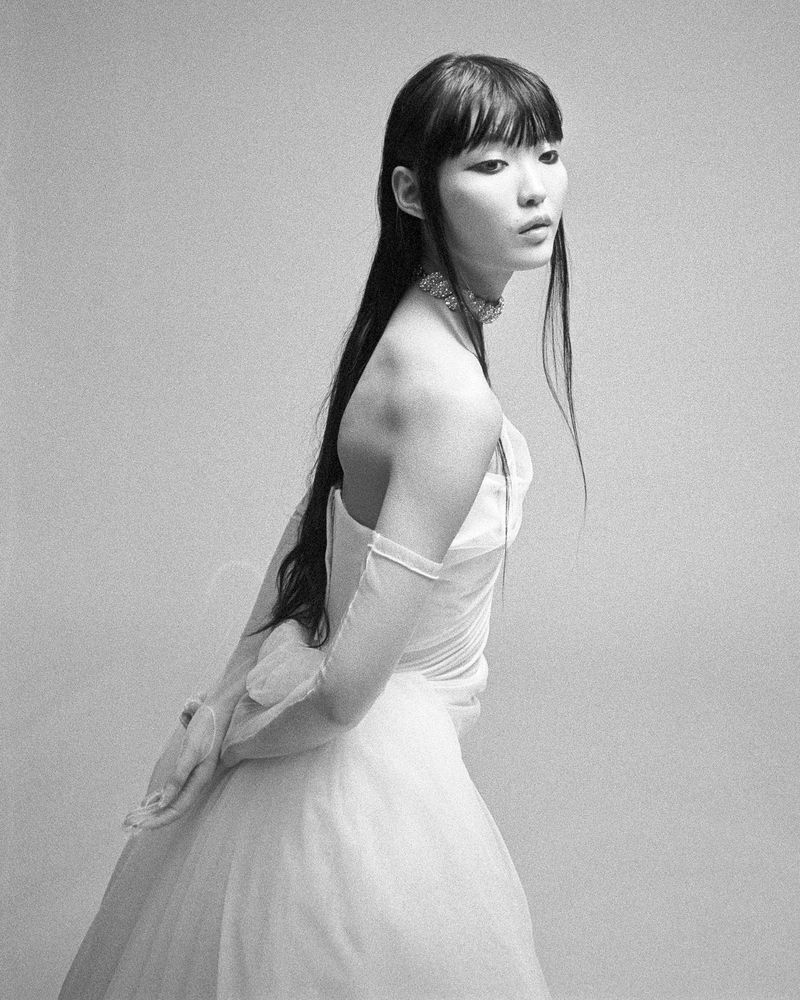 Portrait of an Asian woman in a white dress and long black hair against a neutral background in a studio setting. Minimalist fashion.