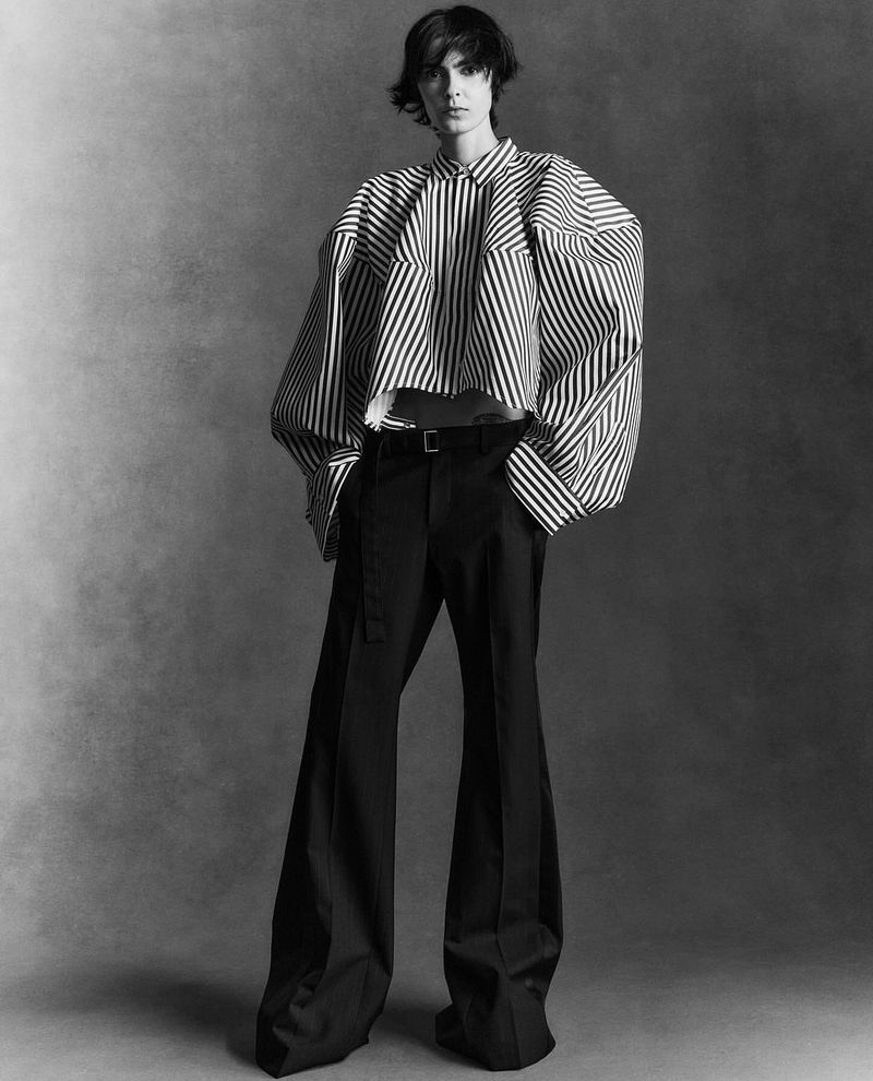 Fashion portrait of a woman in a striped blouse and wide-leg pants against a neutral gray backdrop in a studio setting.