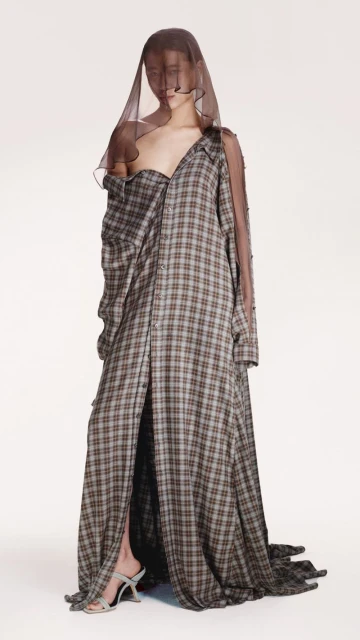 Full-length shot of a model wearing a plaid shirt dress and veil, set against a white backdrop in a fashion studio.