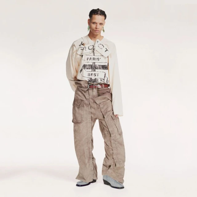 Full shot of person in tan long-sleeve shirt with graphic print and wide-leg cargo pants against a white backdrop in a studio.