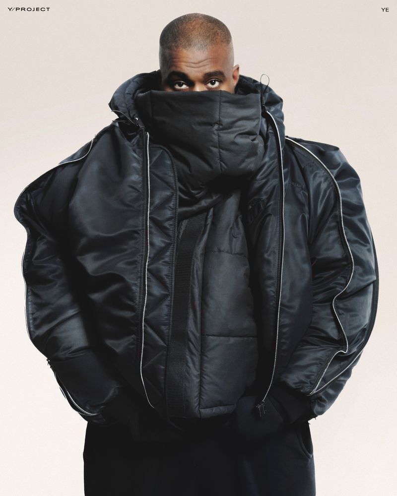 Portrait of a bald adult male wearing a large, black hooded puffer jacket that covers most of his face against a light backdrop.