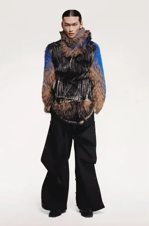 Model wearing a textured blue and brown layered jacket and dark trousers against a white background