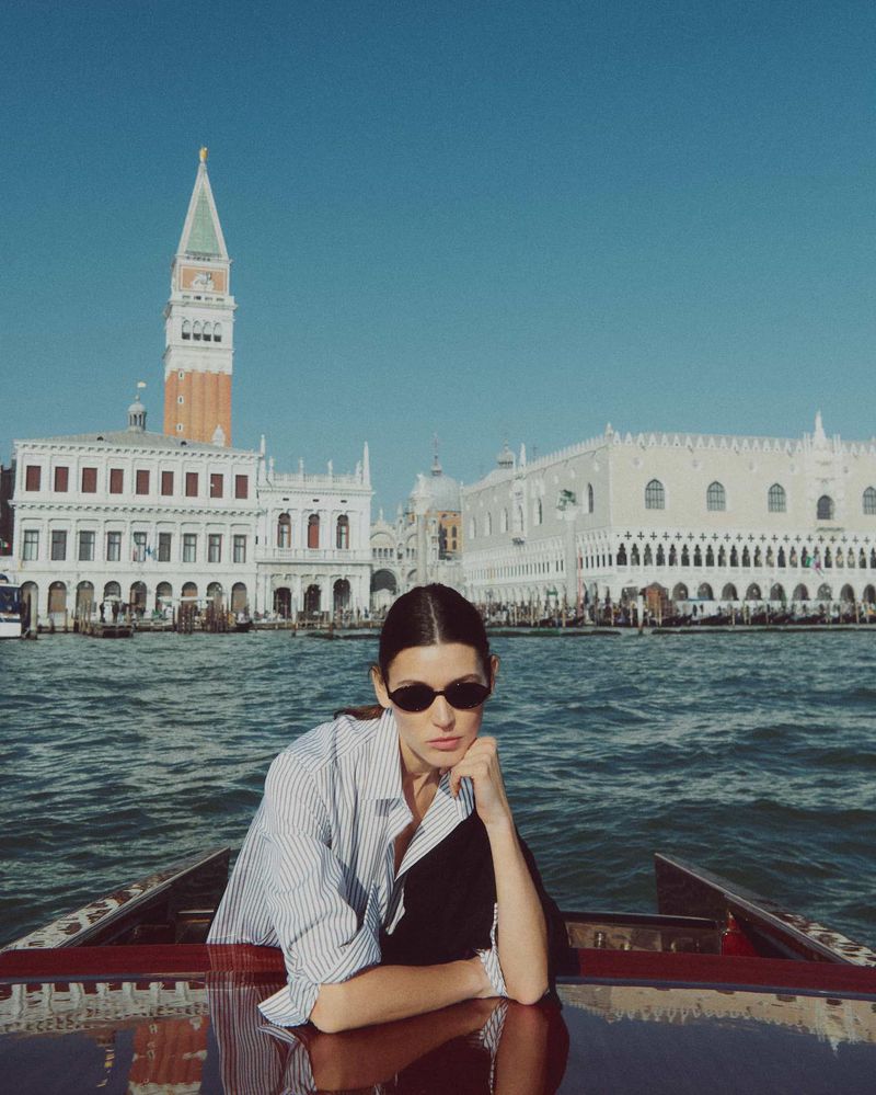 A woman in a boat on a canal in Venice, Italy, with historic buildings and the Campanile di San Marco in the background.