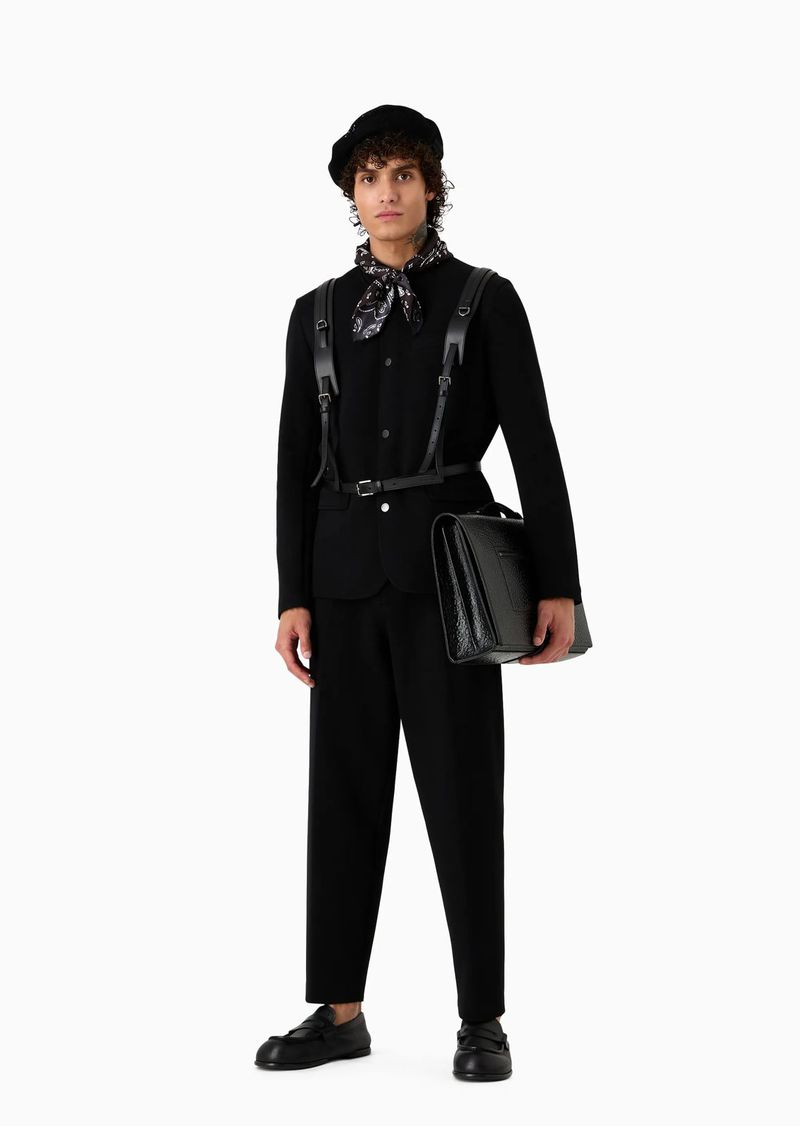 A single adult male stands in a full shot against a white backdrop, wearing a black beret, jacket, pants, and shoes, with a patterned ascot.