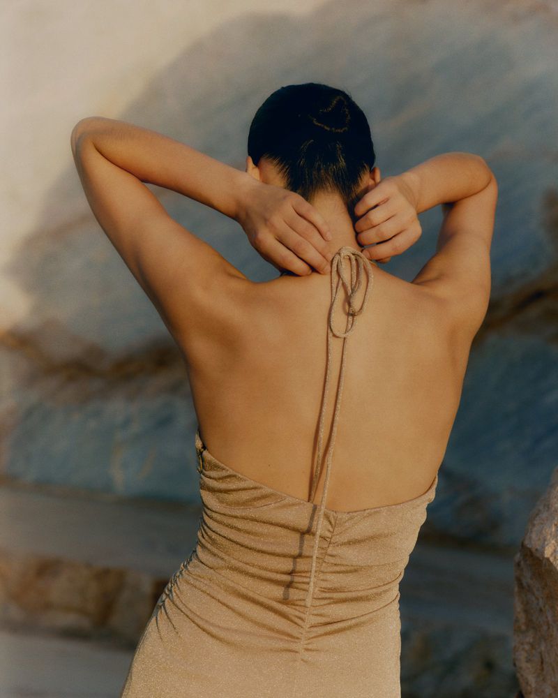Model seen from behind wearing a halter neck dress outdoors against a rocky natural backdrop for ME+EM April 1 Lookbook