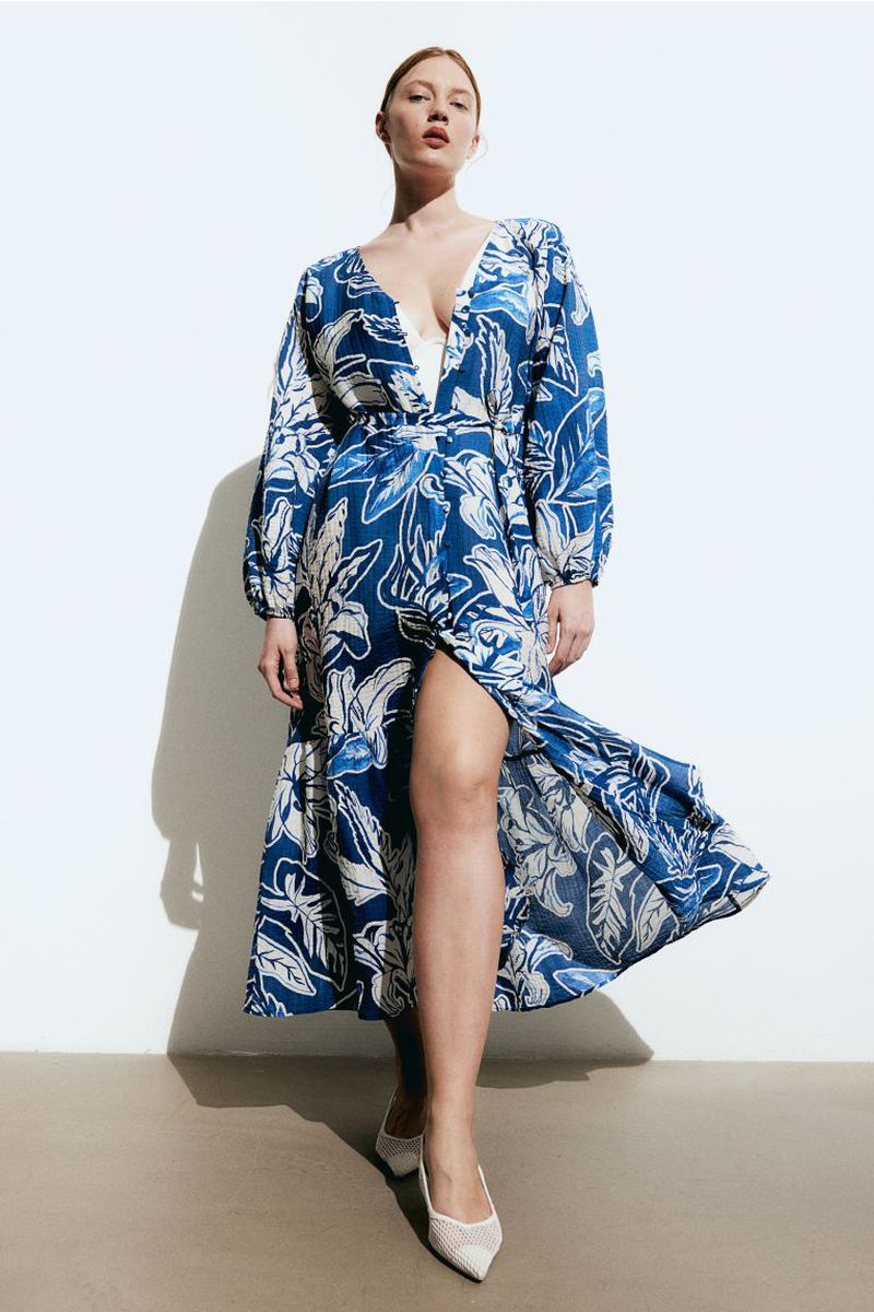 Woman in floral wrap dress and white heels posing in front of a white background in a studio, fashion editorial shot, full length.