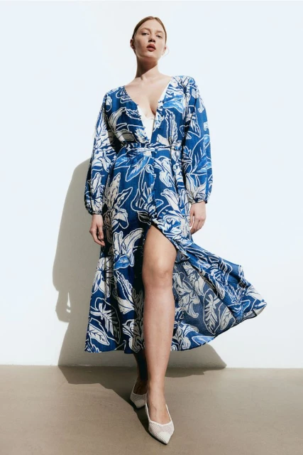 Woman in floral wrap dress and white heels posing in front of a white background in a studio, fashion editorial shot, full length.