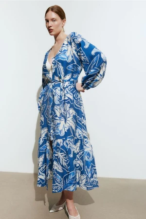 Model wearing a blue and white patterned floral maxi dress posing against a plain neutral background.