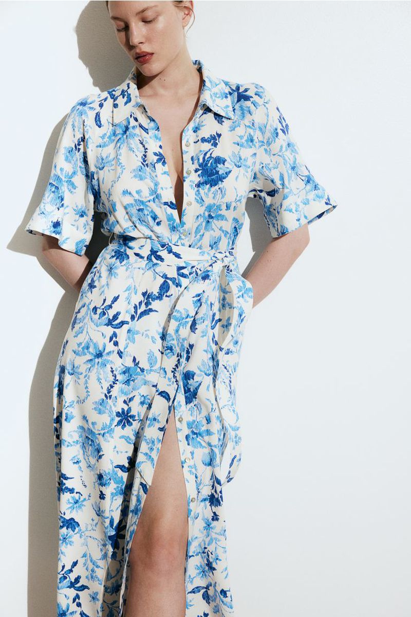 Adult woman poses in long-sleeved floral midi dress with a thigh-high slit against a white background in a studio with diffused lighting.