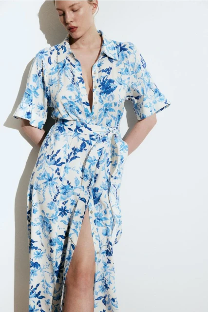 Adult woman poses in long-sleeved floral midi dress with a thigh-high slit against a white background in a studio with diffused lighting.