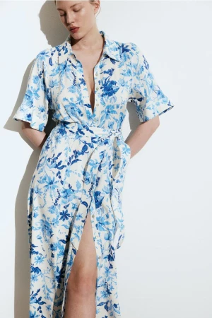 Adult woman poses in long-sleeved floral midi dress with a thigh-high slit against a white background in a studio with diffused lighting.