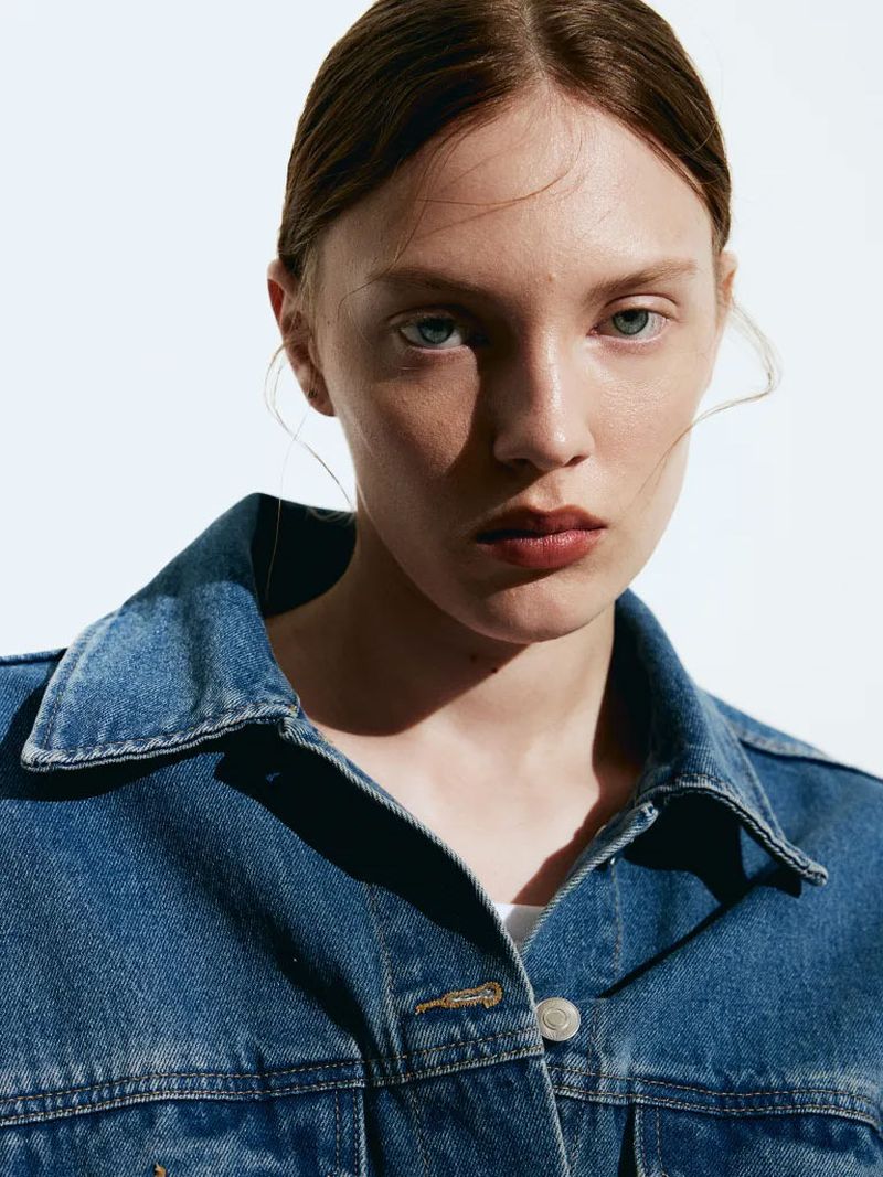 Close-up portrait of a woman wearing a blue denim jacket against a bright white background