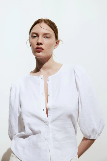 Fashion portrait of a fair-skinned woman wearing a white button-down shirt, posing against a bright white background in the photo studio.