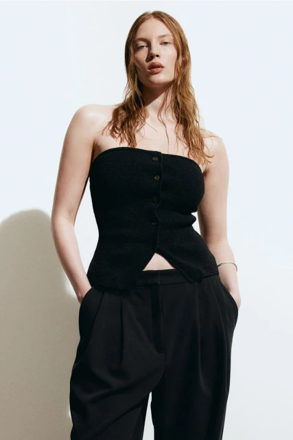 A red-haired woman poses in a black tube top and black pants against a white backdrop in a fashion studio shot.
