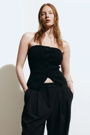 A red-haired woman poses in a black tube top and black pants against a white backdrop in a fashion studio shot.