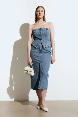 Model wearing a denim bustier top and matching skirt holding a white handbag in a studio