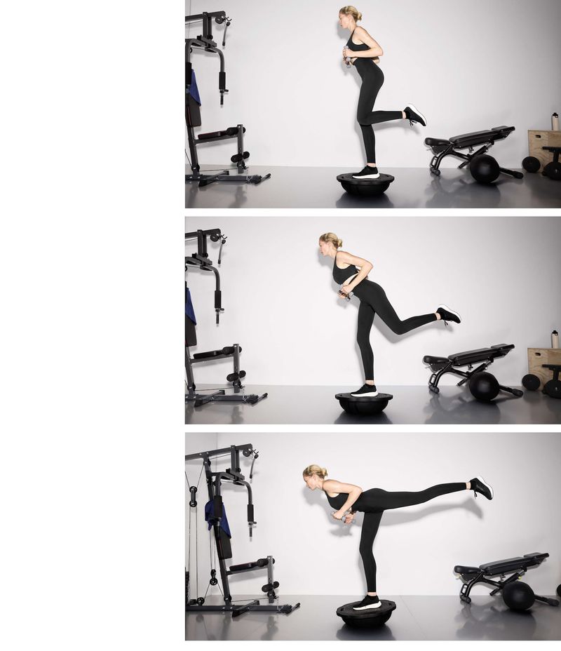 Adult woman in fitness apparel performing balance exercise on a Bosu ball in a bright, minimalist indoor gym setting with workout equipment.