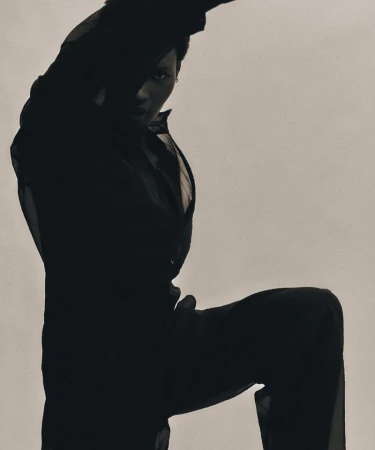 Model Nyarach Abouch Ayuel in a black sheer shirt and trousers posing against a grey seamless background