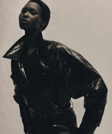 Model wearing a glossy dark trench coat posing against a plain neutral background for BOSS.