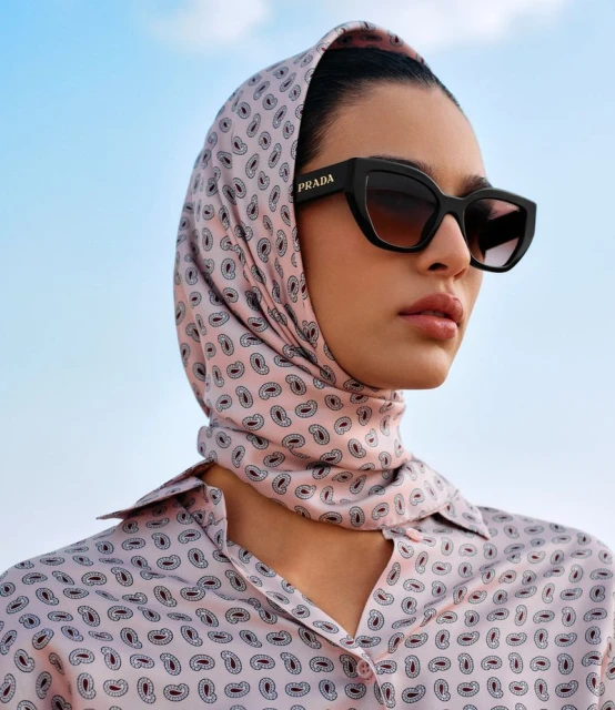Close-up of a woman wearing a patterned scarf and sunglasses, showcasing a blend of fashion and outdoor style with a clear sky.