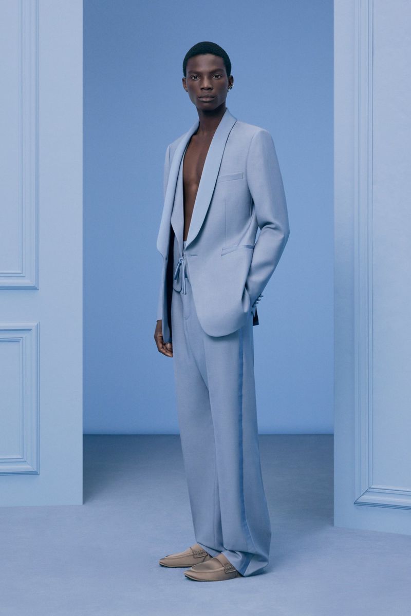 Elegant Black male model in light blue suit poses in a doorway on a matching blue background, highlighting high fashion and modern style.