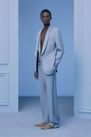 Elegant Black male model in light blue suit poses in a doorway on a matching blue background, highlighting high fashion and modern style.