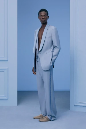 Model wearing a light blue suit jacket and matching trousers against a pale blue studio background
