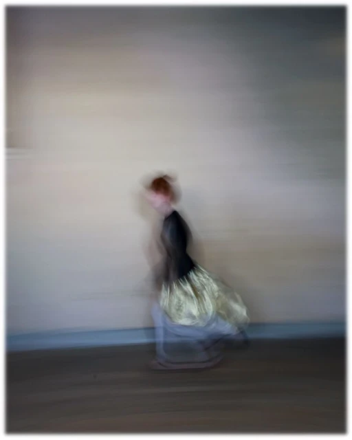 Blurred motion shot of a child in a black and gold dress running indoors with neutral wall and dark floor, abstract motion blur effect.