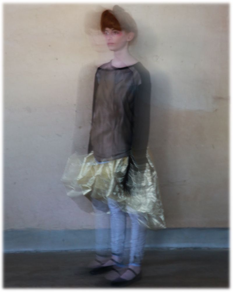 Fashionable woman poses in a studio wearing a brown long-sleeve shirt, light colored jeans, ballet flats, and a gold ruffled skirt.