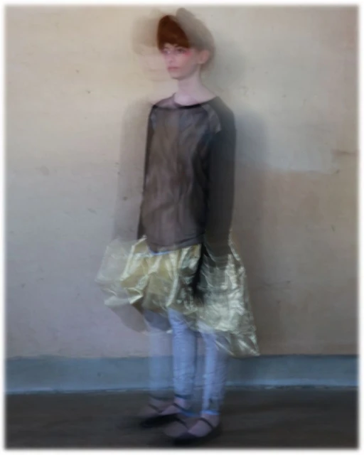 Fashionable woman poses in a studio wearing a brown long-sleeve shirt, light colored jeans, ballet flats, and a gold ruffled skirt.