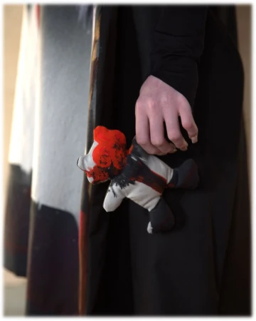 Close-up of a person's hand holding a handmade plush toy with black and red paint on a white background, showcasing texture and design.