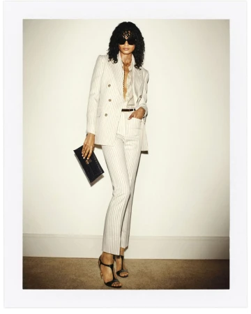 Model in pinstripe suit and sunglasses holding a black clutch against a plain white wall for Tom Ford S/S 24