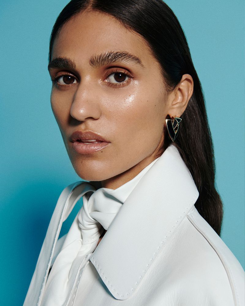 Portrait of an adult female with brown hair, wearing a white jacket, posing against a blue background in a fashion-style photo.