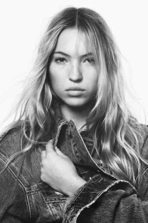 Model Lila Moss looking directly forward while wearing an oversized denim jacket in a black and white studio portrait.