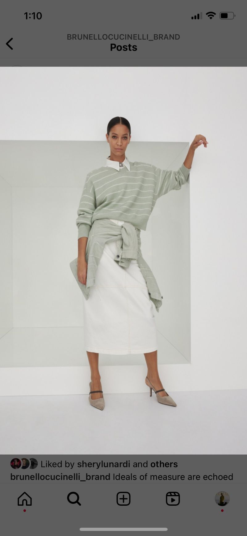 Fashionable adult woman posing in front of a white wall wearing a white skirt, a striped sweater and brown heels.
