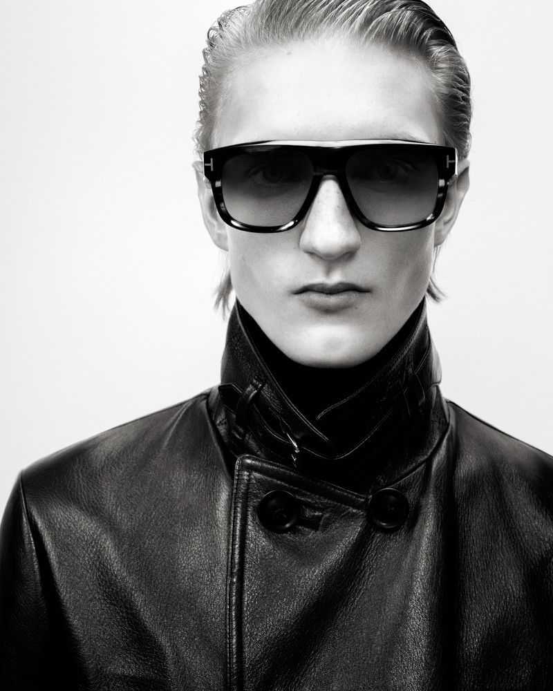 Black and white portrait of an adult wearing black leather jacket and sunglasses on a light background, fashion studio shot.