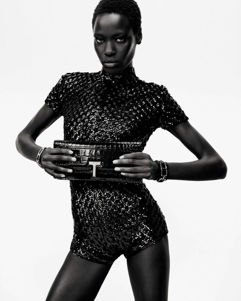 Fashion shot of a Black woman in a black sequined romper holding a black purse with a silver logo on a bright white background.
