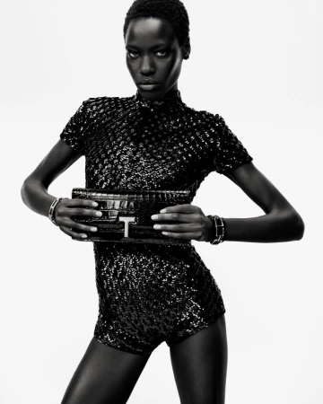 Awar Odhiang poses in a black sequin romper holding a black crocodile leather clutch against a white seamless background.