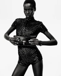 Awar Odhiang poses in a black sequin romper holding a black crocodile leather clutch against a white seamless background.