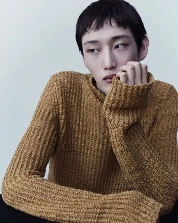 Model wearing a textured mustard yellow knit sweater against a plain neutral background