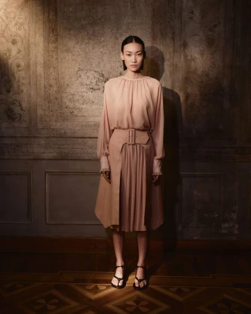 Full-length portrait of an adult female fashion model posing in a long-sleeve top and skirt in a photo studio with patterned flooring.