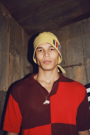 Model wearing a color-blocked shirt and a yellow cap inside a rustic wooden room