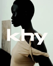 Model Mimi Arok in a beige off-the-shoulder top in profile with bold white Khy lettering overlaid.