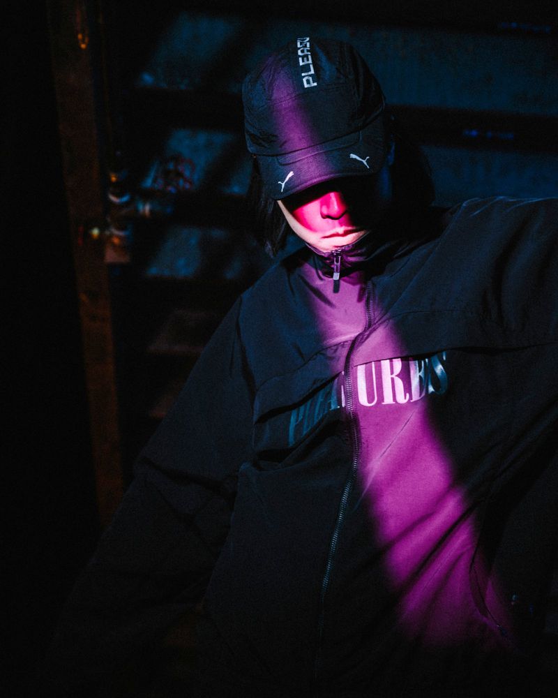 Person in black Puma cap and jacket under neon light. Dark, urban fashion shot.  Streetwear style. Fashionable outdoor portrait.